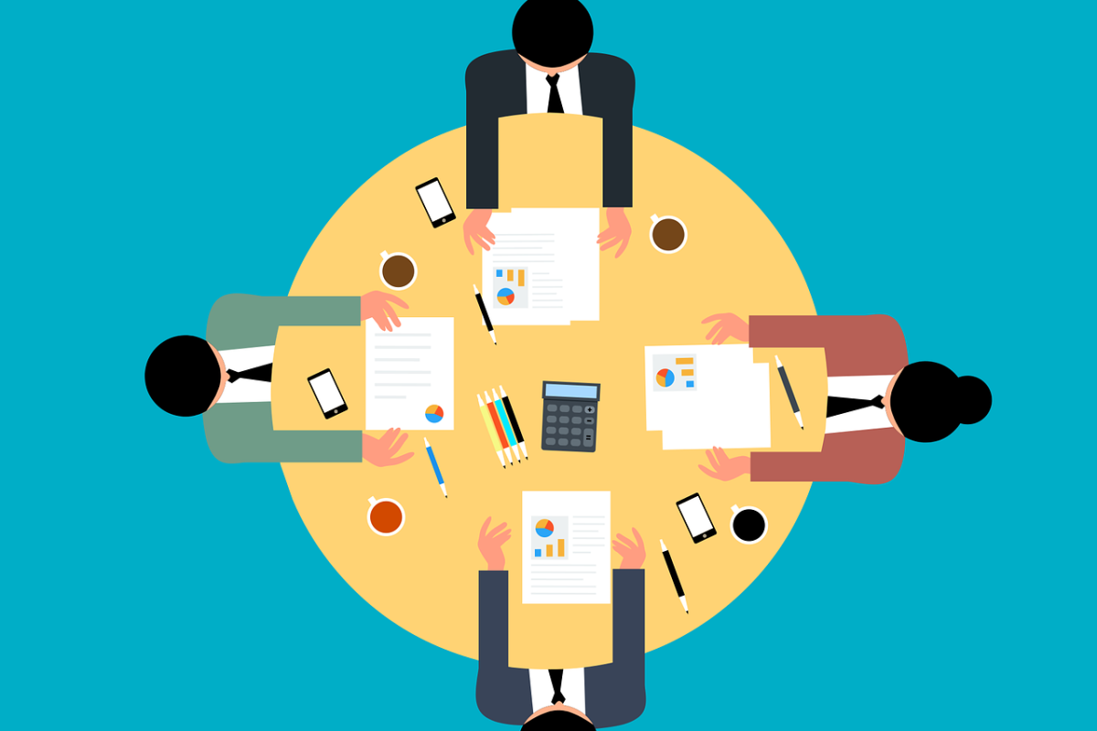 Cartoon image of four people sat around a yellow table with papers in front of them. Image perspective is from above.